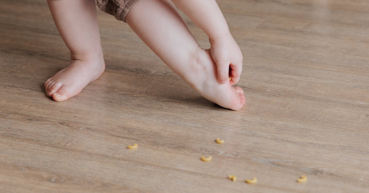 How can I remove arrows stuck in a player? - Crop faceless toddler standing barefoot on floor and trying to remove stuck pasta from foot while playing and developing fine motor skills at home