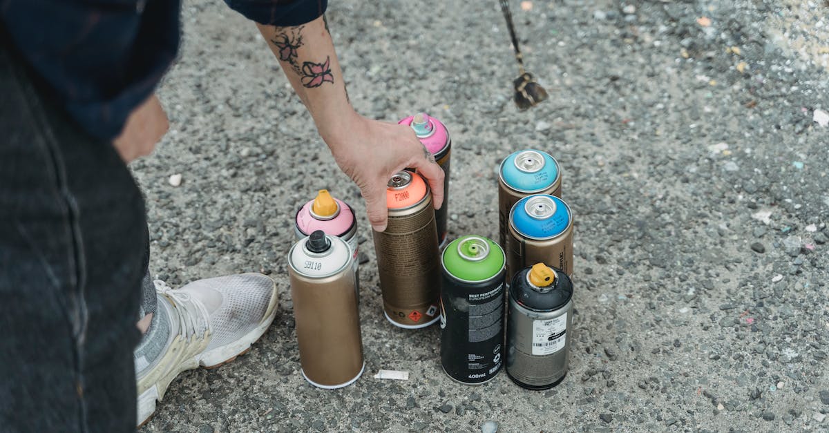 How can I upgrade my skills? - Crop faceless tattooed artist taking paint bottle from heap of multicolored spray cans placed on ground on street of city