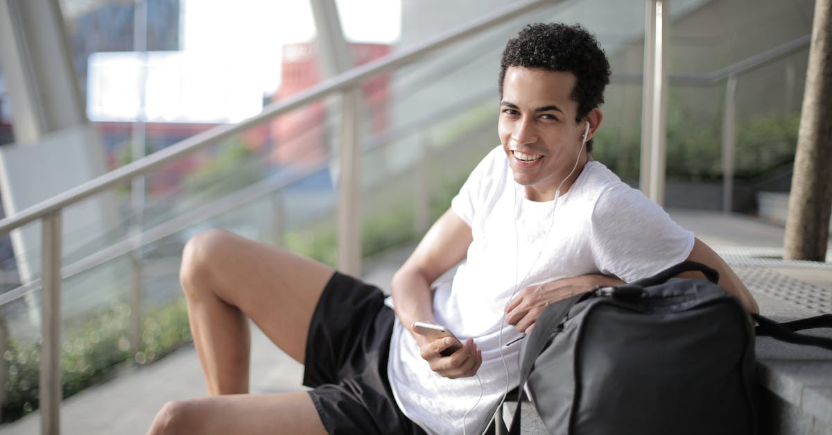 How can I use the BANNED PUBG Mobile in India? - Delighted African American man in earphones and sportswear smiling at camera while sitting with big black bag on stairs and listening to music against blurred exterior of contemporary building in city How can I use the BANNED PUBG Mobile in India? - Delighted African American man in earphones and sportswear smiling at camera while sitting with big black bag on stairs and listening to music against blurred exterior of contemporary building in city