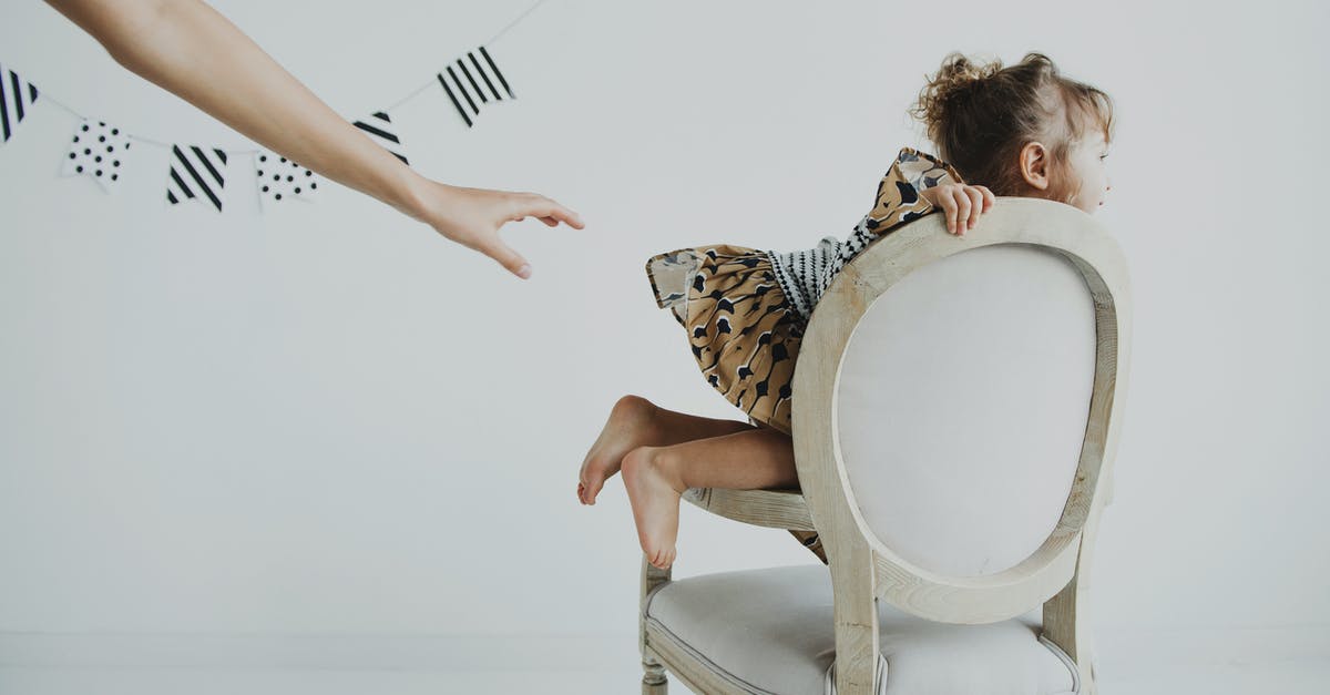 How can I view the contents of my controller pak? - Side view of crop faceless person reaching out hand to cheerful little female child in dress sitting on classic chair in light studio with garland on wall and looking away