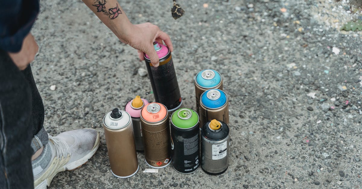 How can many Puddle Slimes can be in a pond together without blushing? - Crop anonymous person in sneakers with tattoo and heap of multicolored spray paint cans on ground standing on street in city
