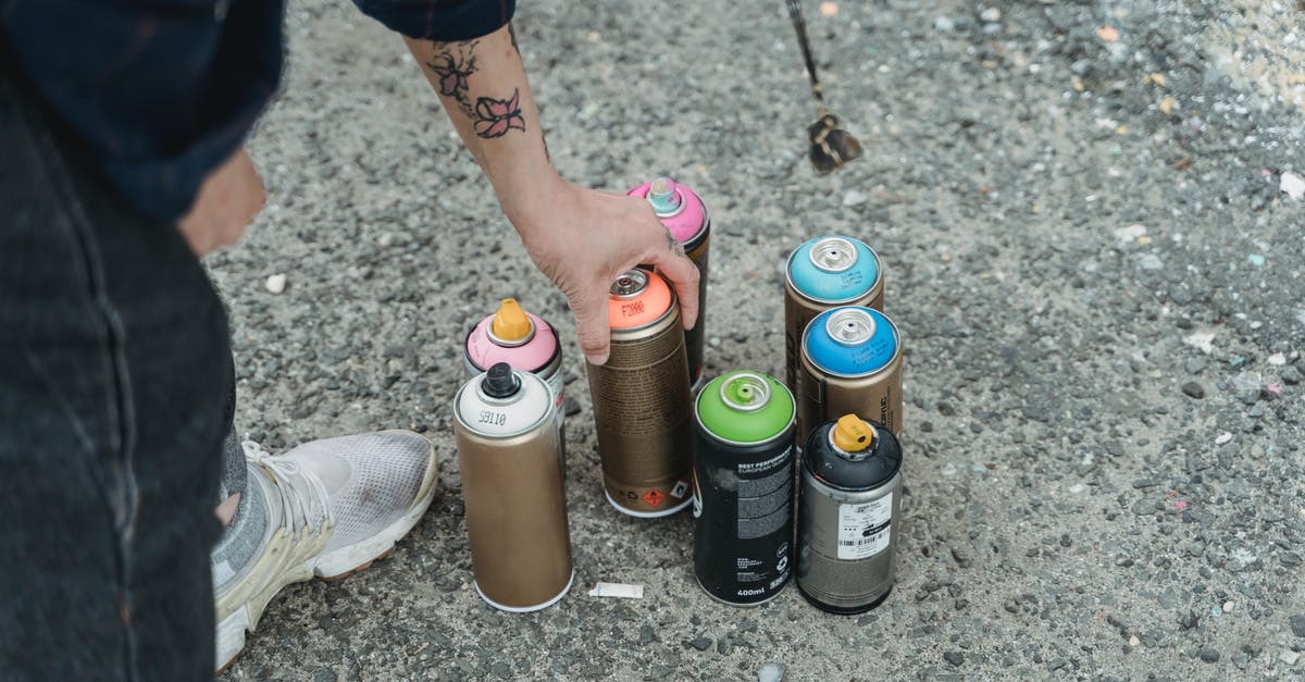 How can many Puddle Slimes can be in a pond together without blushing? - Crop faceless tattooed artist taking paint bottle from heap of multicolored spray cans placed on ground on street of city