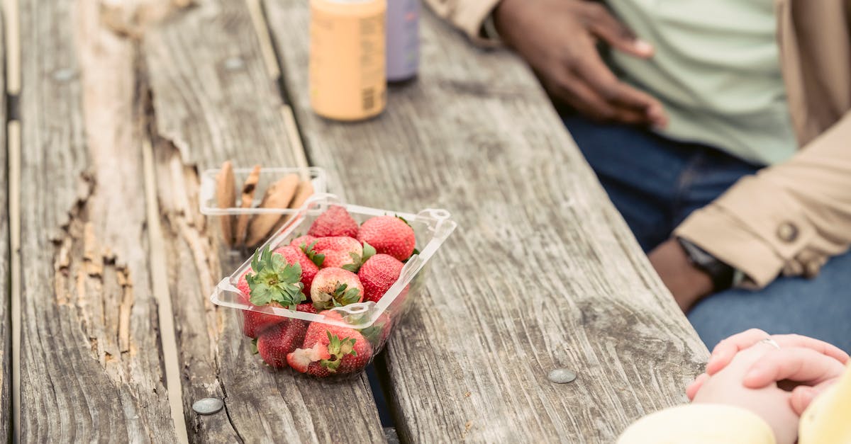 How can you upgrade multiple units at the same time? - Crop anonymous couple sitting at shabby wooden table with strawberries and cookies near cans of soda while spending time in park
