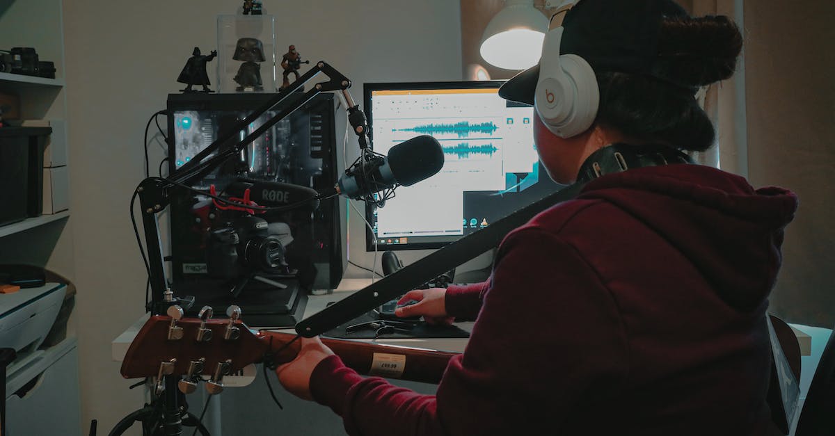 How can you use headsets with separate Audio and Mic cables for Dualshock4? - Back view faceless musician with guitar in casual wear and headphones sitting at table with computer and microphone while recording music