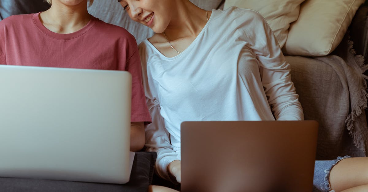 How close must my friends be in order to trade in Pokémon Home? - Crop happy Asian girlfriends working on laptops and smiling while sitting together on floor in cozy room with sofa
