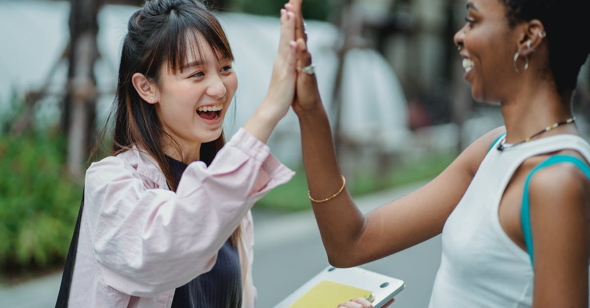How did my friend get a backpack with 98/33 items? - Side view excited multiracial female students in casual clothes giving high five to each other while spending break in lush park