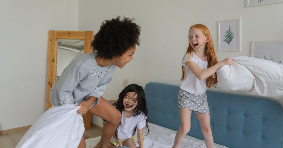 How did this action have that consequence? - Cheerful girls fighting with pillows on bed How did this action have that consequence? - Cheerful girls fighting with pillows on bed