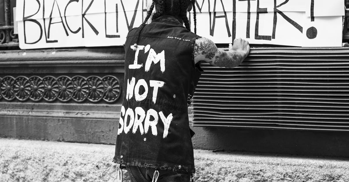 How do I acquire Outfit Vouchers? - Back view of unrecognizable tattooed guy standing on street in front of banner with Black Lives Matter inscription