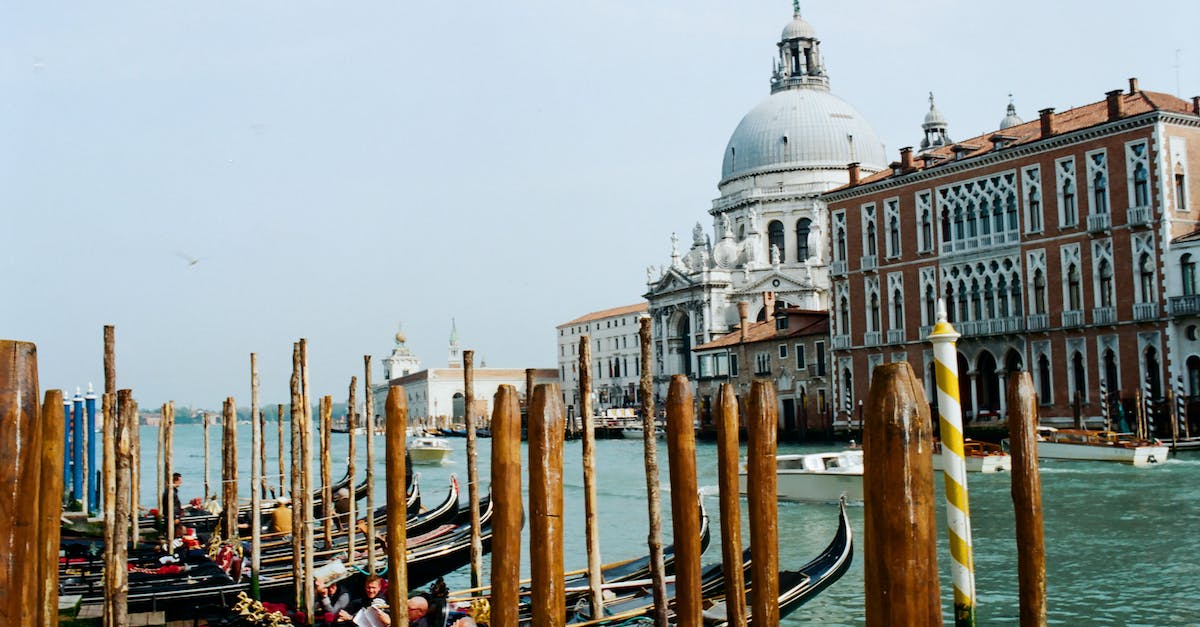 How do I add a tourist to a vessel in KSP - Dock with gondolas with wooden pillars moored on calm sea water against aged building with dome against cloudless blue sky in Venice