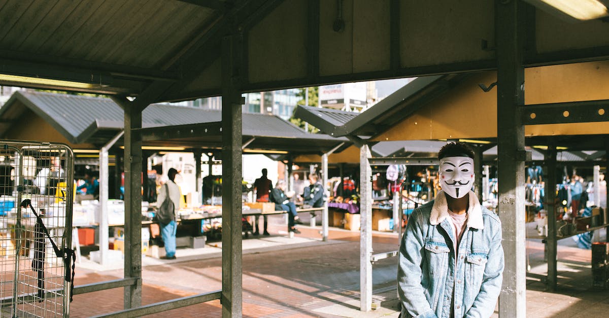How do I change my appearance? - Unrecognizable black man in stylish clothes and Anonymous mask standing in local market in city and looking at camera in sunny day