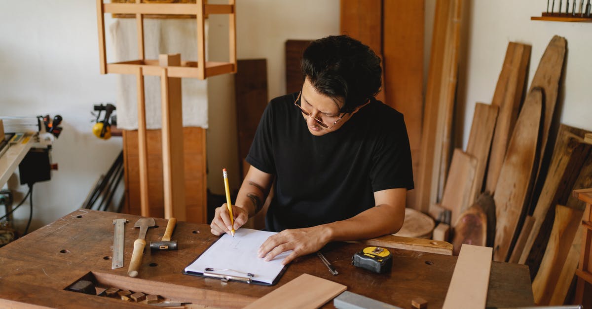 How do I create a feudal vassal as a tribal ruler? - Concentrated man in glasses sitting at wooden table in workshop and holding pencil while creating new object on paper
