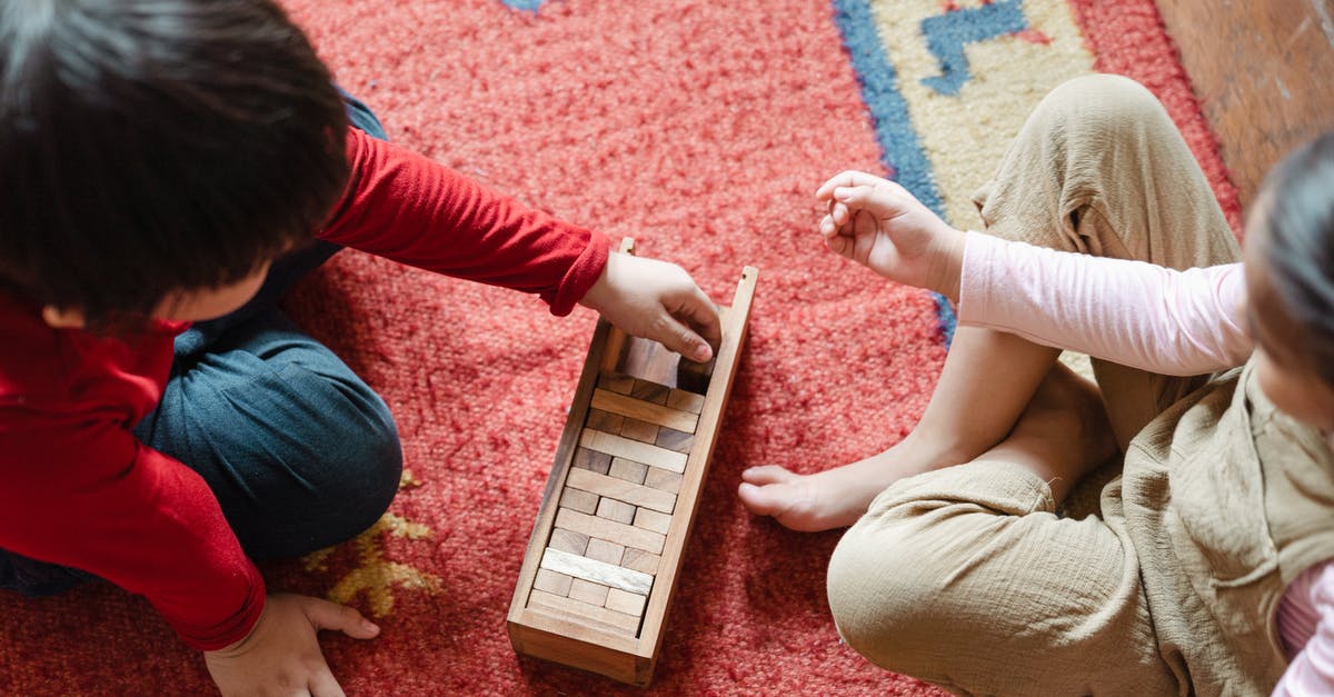 How do I create unbreakable blocks? - Top view of anonymous barefoot boy and girl in casual clothes sitting on floor carpet and playing with wooden blocks of jenga tower game