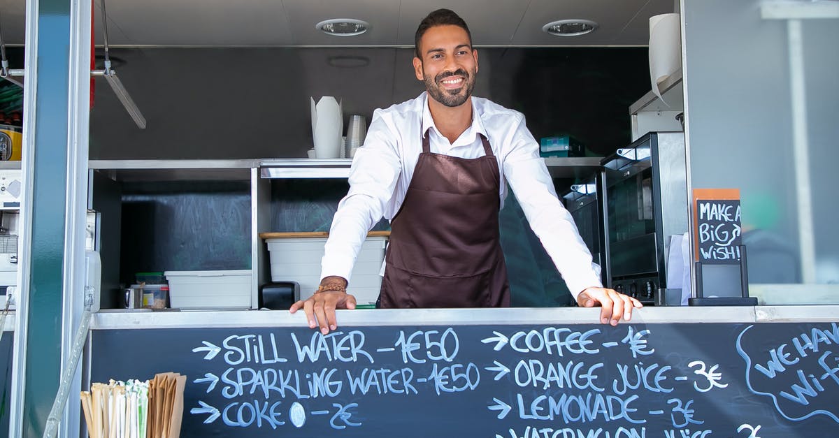 How do I detach a trailer from a tractor? - Low angle of ethnic seller wearing uniform standing at counter in food trailer and smiling happily