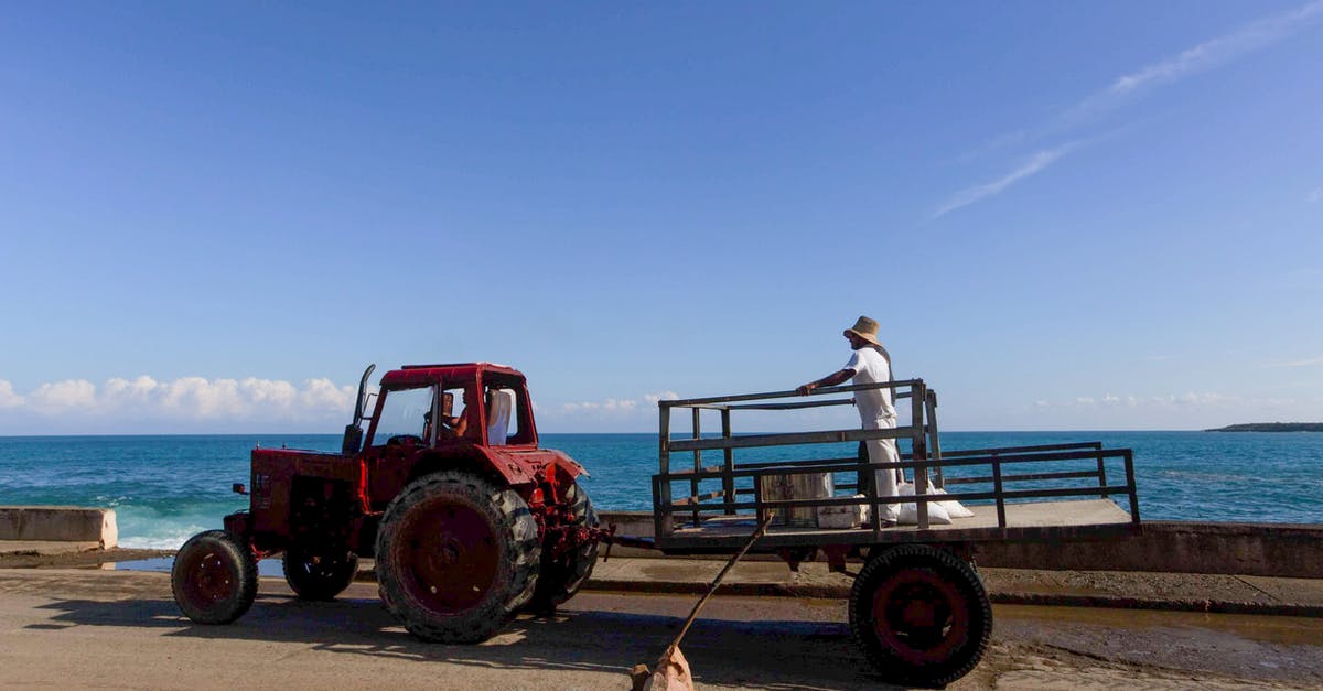 How do I detach a trailer from a tractor? - Man in White Shirt and Blue Denim Jeans Sitting on Red Tractor