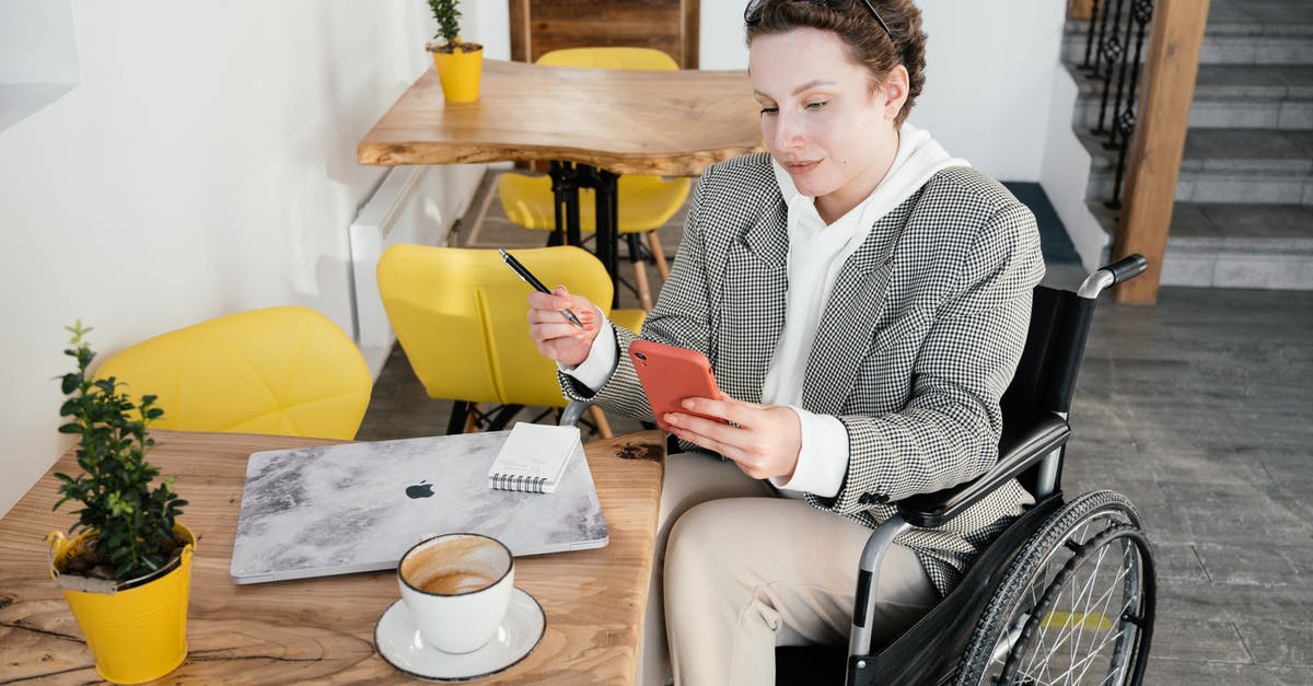 How do I disable Ubisoft Connect popups? - High angle of focused female in wheelchair browsing cellphone at table with netbook and cup of latte