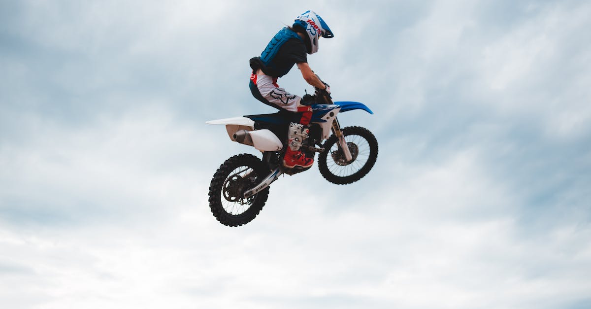 How do I get a lot of Stunt Driver points? - Side view of anonymous male biker in helmet on motorcycle doing trick while jumping high into air against cloudy sky in daylight