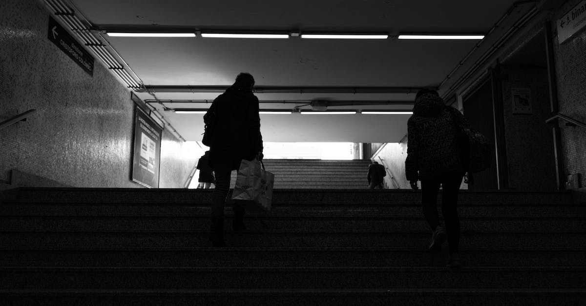 How do I go up staircases? - Back view black and white of anonymous passengers walking up staircase leaving subway station