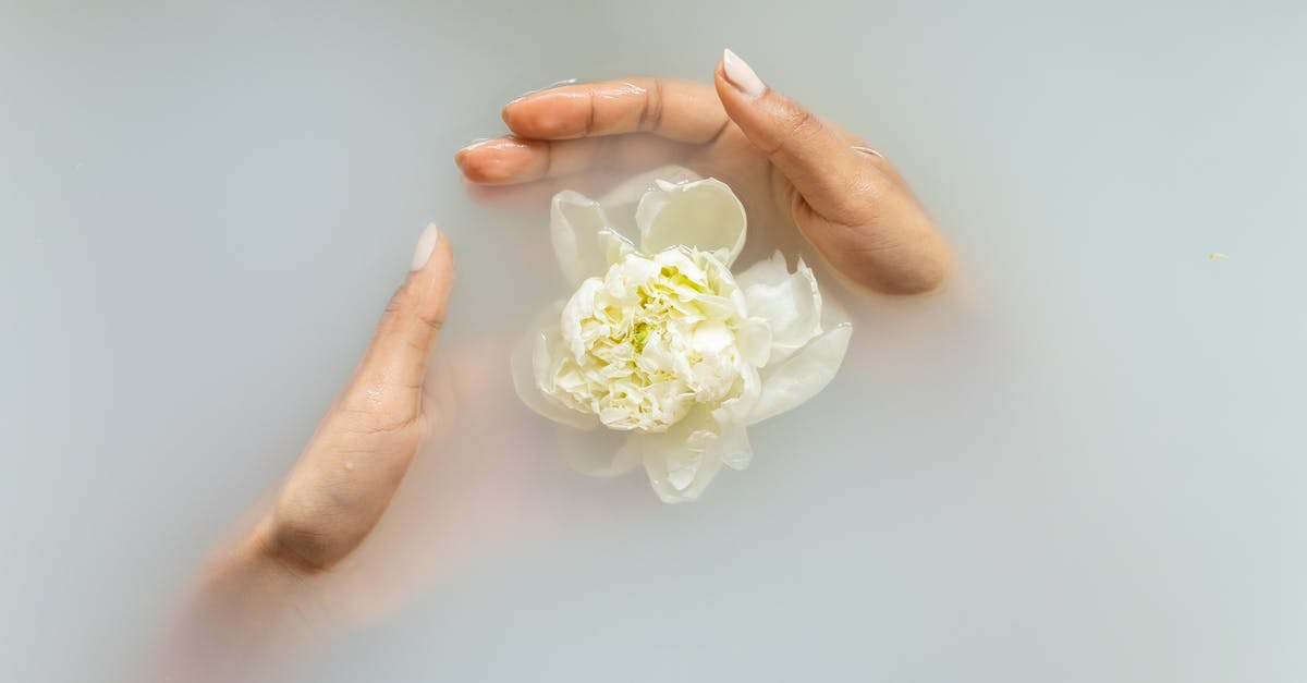 How do I heal land-armies? - Unrecognizable female with manicured hands holding white flower in hands in soapy water during spa procedures