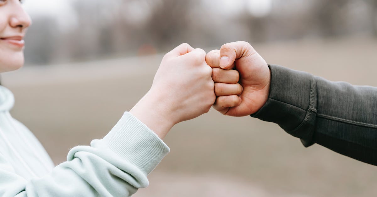 How do I help my party achieve their dreams? - Crop anonymous cheerful woman and man giving fist bump to each other on blurred background of park