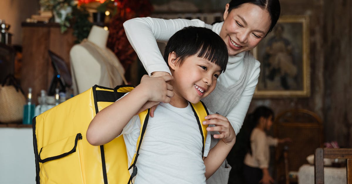 How do I help my staff be happy? - Happy female cafeteria employee putting on big yellow thermo bag on shoulders of positive child in casual wear working as food courier and looking away