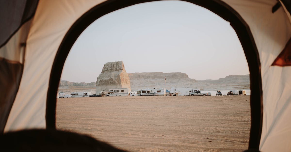 How do I open this door on the west coast? - View of sandy beach with distanced cars parked on seaside with rocky cliffs through opened tent in nature with cloudless sky