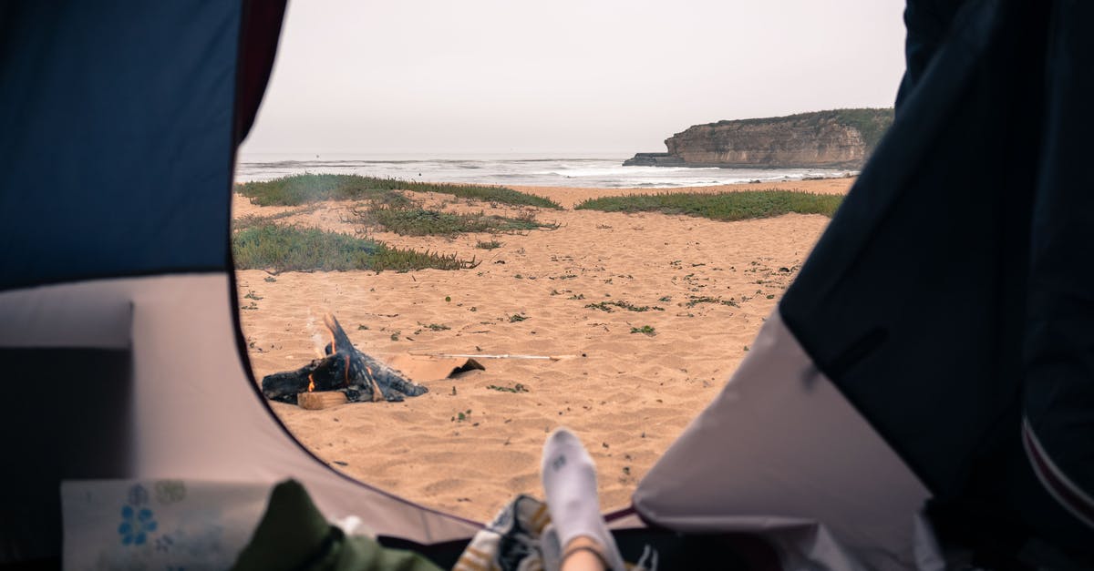 How do I open this door on the west coast? - Unrecognizable tourist resting in tent with opened door in nature on sandy seashore with rippling sea and rocky cliff in distance How do I open this door on the west coast? - Unrecognizable tourist resting in tent with opened door in nature on sandy seashore with rippling sea and rocky cliff in distance