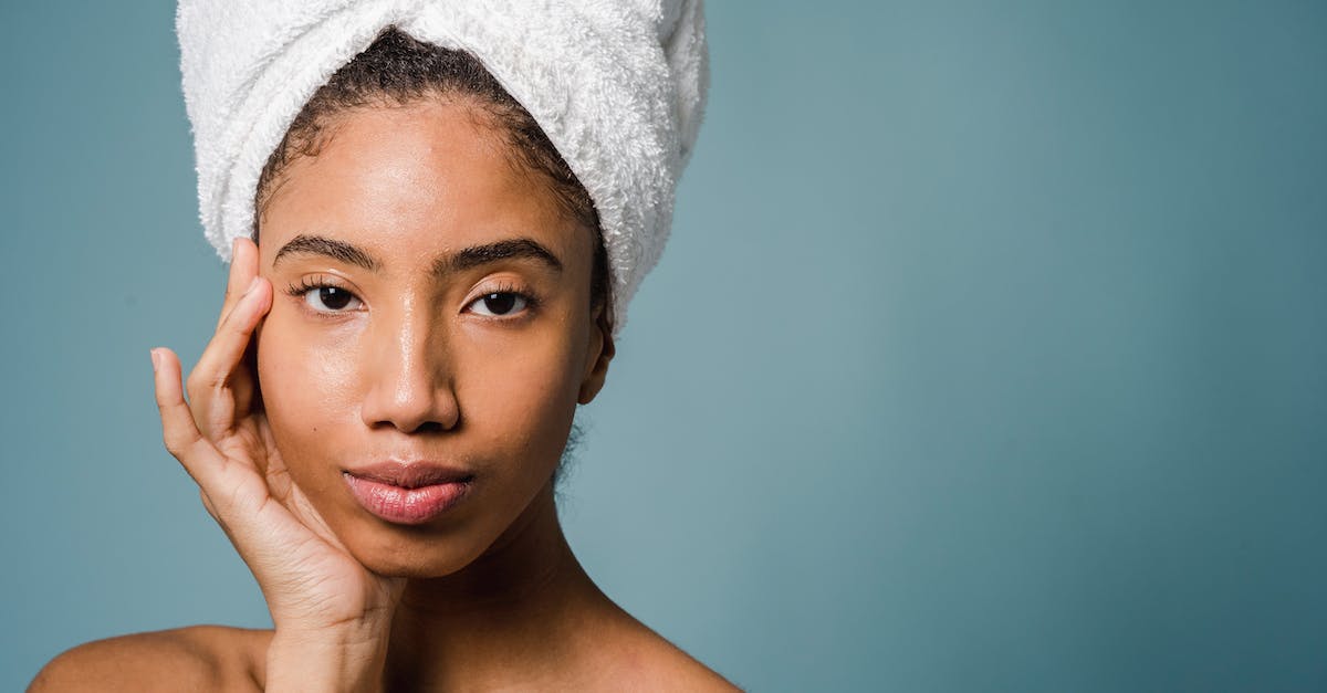 How do I perfect my gemology? - Tranquil young black female with pure skin and white towel on head touching face and looking at camera after spa procedures against blue background How do I perfect my gemology? - Tranquil young black female with pure skin and white towel on head touching face and looking at camera after spa procedures against blue background
