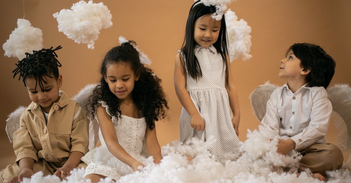 How do I play Halo 4 against bots? - Positive multiracial children in angel outfits with halo and wings playing with decorative with cotton wool while sitting on brown background