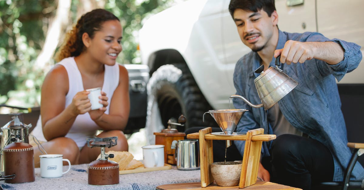 How do I prepare for summer heat? - Cheerful young multiracial couple in casual clothes pouring boiling hot water into pour over filter while having coffee break together in sunny nature
