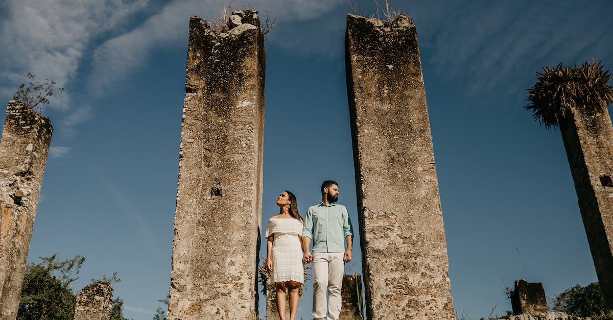 How do I proceed past this location with an eye and a blocked door? - From below full body of male and female standing together near remains of ancient building and holding hands while looking away in sunny day How do I proceed past this location with an eye and a blocked door? - From below full body of male and female standing together near remains of ancient building and holding hands while looking away in sunny day