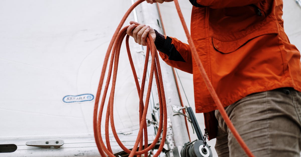 How do I repair a damaged sailing boat? - Person in Orange Jacket Holding Brown Hose