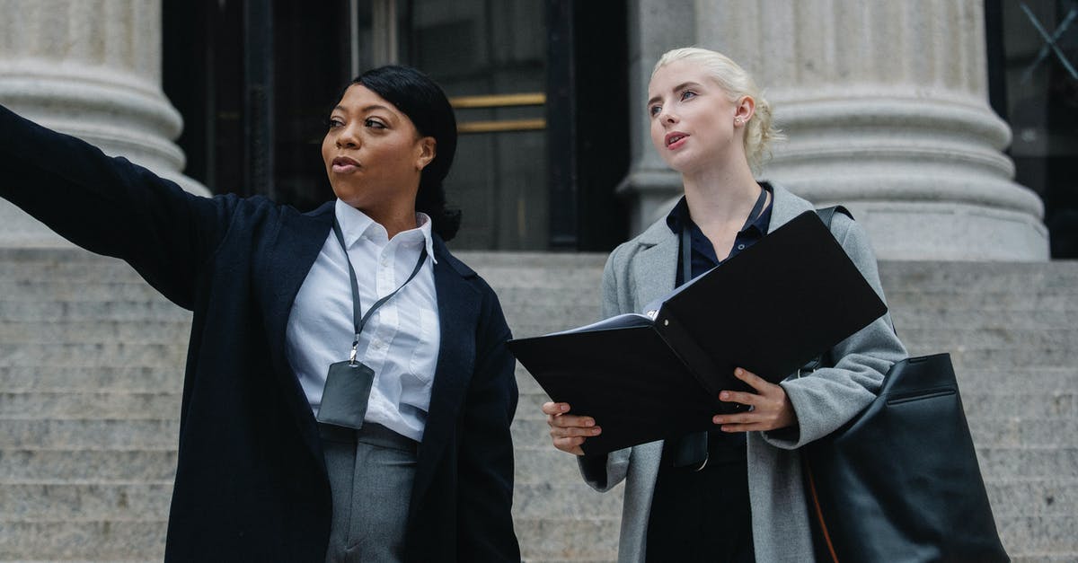 How do I score contract bonus points? - Low angle of African American lady formal outfit and badge pointing away while standing on street with female colleague with documents folder How do I score contract bonus points? - Low angle of African American lady formal outfit and badge pointing away while standing on street with female colleague with documents folder