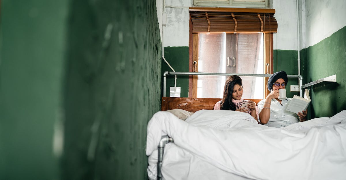 How do I scroll the inventory right in the book store? - Indian couple of wife scrolling through news feed on smartphone and husband enjoying coffee and reading book on wooden bed in room with roughly plastered green walls