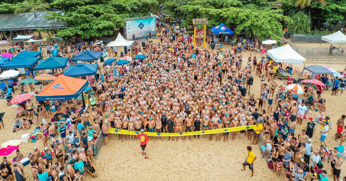 How do I start the crossbow challenge? - Drone view of crowd of people in swimsuits standing behind line tape on sandy beach beginning race