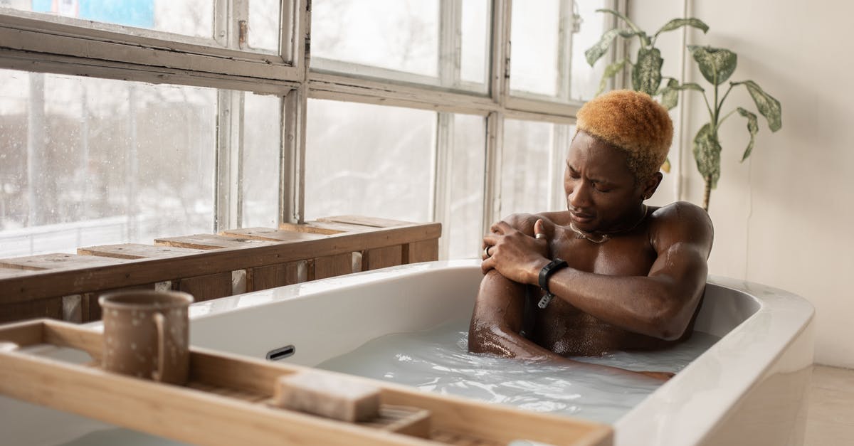How do I take accessories off my slimes? - Young African American man with dyed hair and accessory sitting in bathtub full of water in light room with shabby window frames