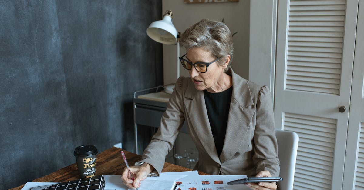 How do I take off a suit in NBA 2K14 my career? - From above of concentrated senior female manager in formal outfit and eyeglasses taking notes in planner while working at table with various documents and takeaway coffee in cozy office