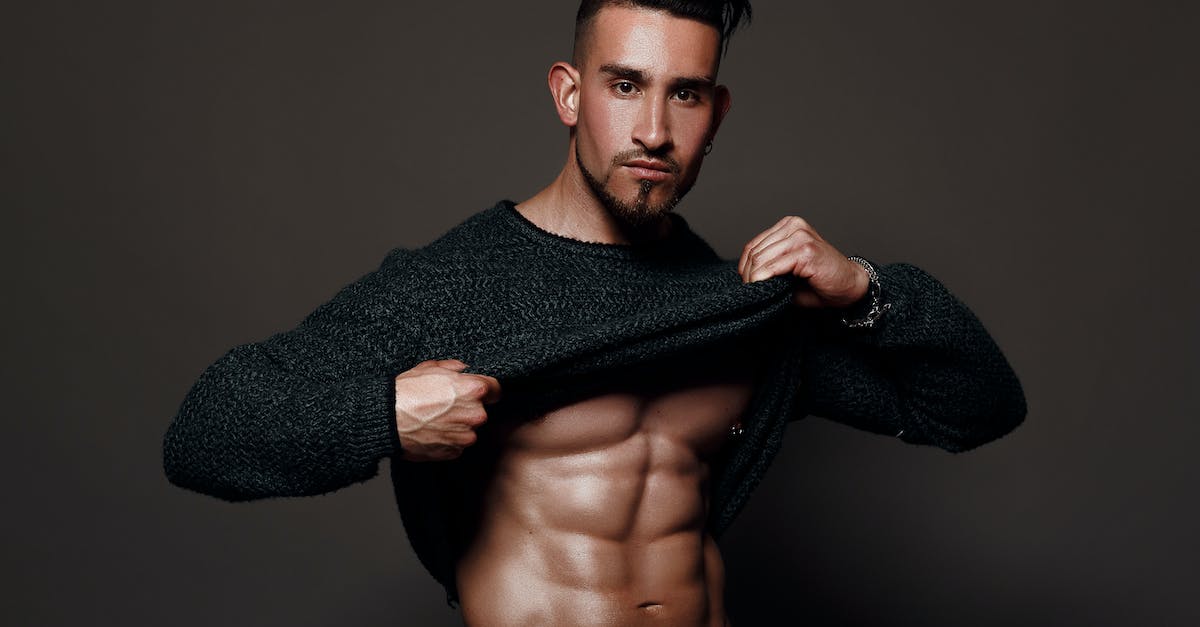 How do I take off body armor? [duplicate] - Muscular male with dark hair and beard standing against gray background and demonstrating torso by taking off sweater