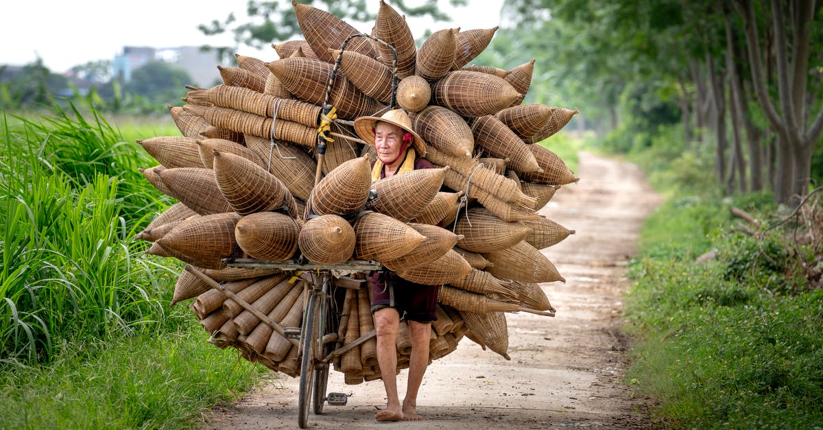 How do I trade with villagers? - Senior Asian man in conical hat and casual clothes carrying bicycle with handmade bamboo fish traps on pathway among green plants in countryside in daytime How do I trade with villagers? - Senior Asian man in conical hat and casual clothes carrying bicycle with handmade bamboo fish traps on pathway among green plants in countryside in daytime