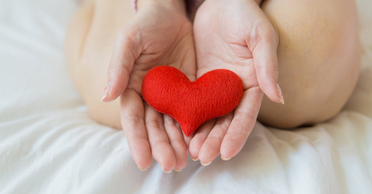 How do NPCs heal our Pokémon? - Unrecognizable female sitting with bare legs on white sheet with small red heart in hands in light room in daytime