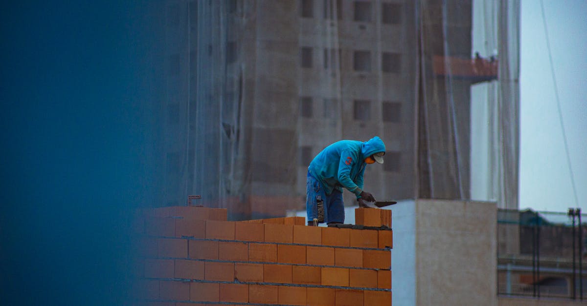 How do you get to build new RZs? - Side view of unrecognizable male in hoodie building brick wall while working on construction site in city How do you get to build new RZs? - Side view of unrecognizable male in hoodie building brick wall while working on construction site in city