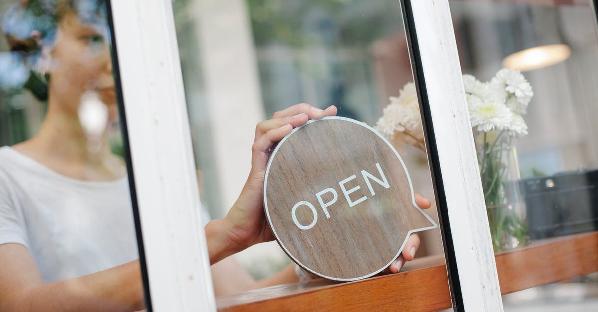 How do you put numbers in a sign or text? - Young woman worker in casual clothes standing in light cafe and putting sign with word open on door