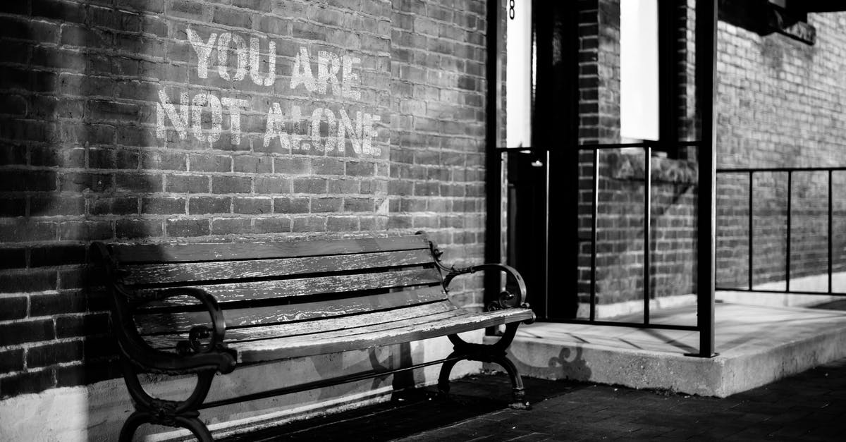 How do you "target" emotes - Black and white of empty wooden bench near brick wall of building with inscription you are not alone