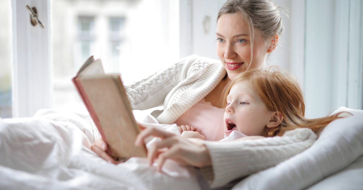 How do you read the radar in multiplayer? - Cheerful young woman hugging cute little girl and reading book together while lying in soft bed in light bedroom at home in daytime