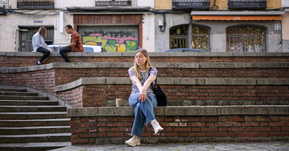 How do you view your town's history when sitting on the wall in the event plaza? - Lonely Blonde Girl Sitting Cross Legged on Wall