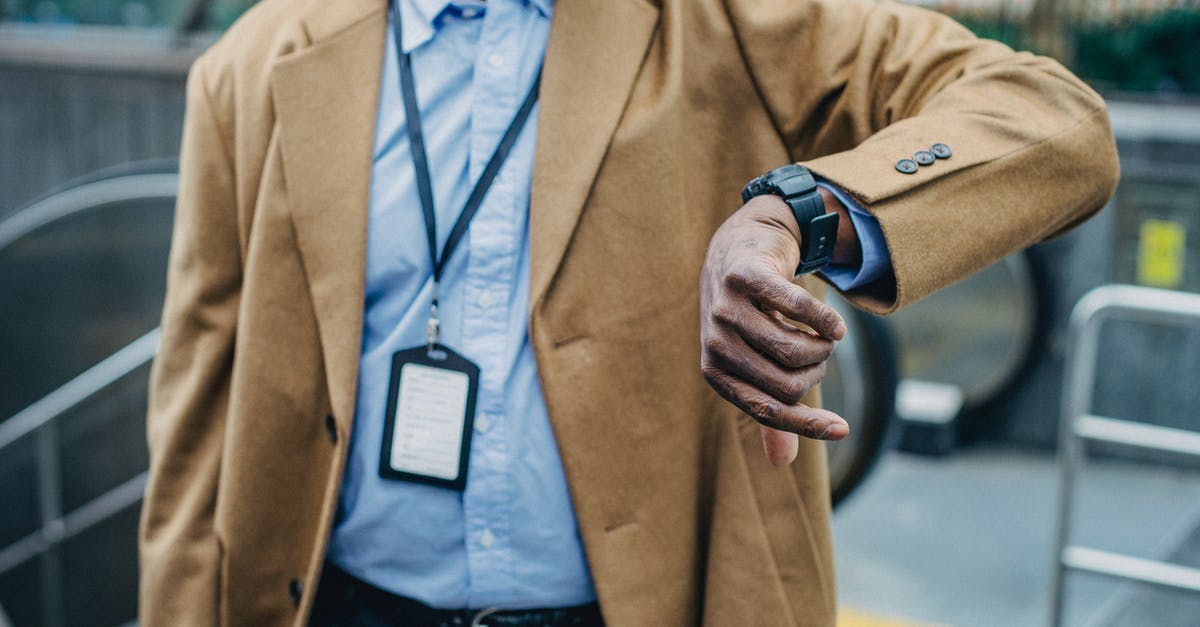 How do you wait until a specific time of day? - Crop anonymous African American businessman in elegant formal suit looking at wristwatch while standing near metro entrance