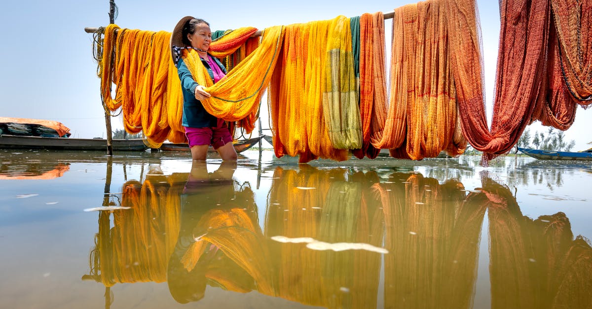 How does a losing battalion choose what province to return to? - Positive middle aged Asian female in casual clothes standing in river water and choosing colorful fishing net hanging on bamboo pole on sunny day in Thua Thien Hue Province