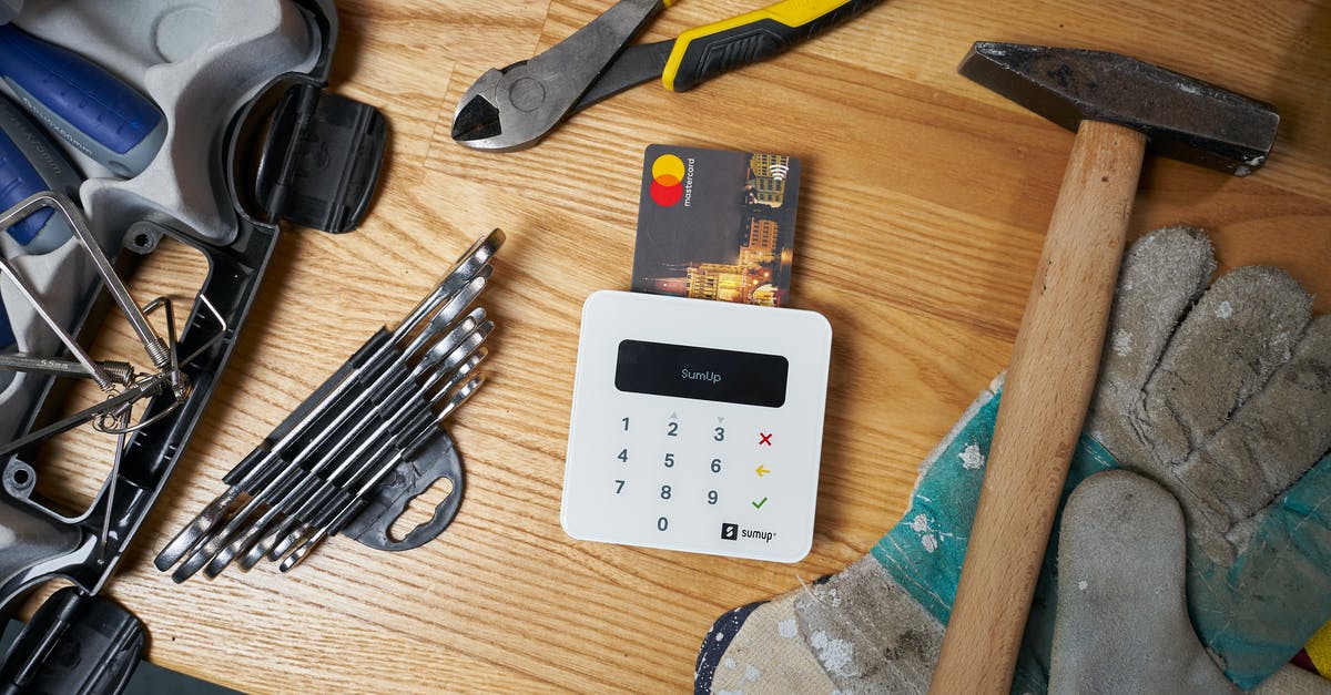 How does item repair work? - Overhead view of bright small plastic card in white contemporary wireless cash register surrounded by screwdriver set and hammer on big dirty gloves next to pliers