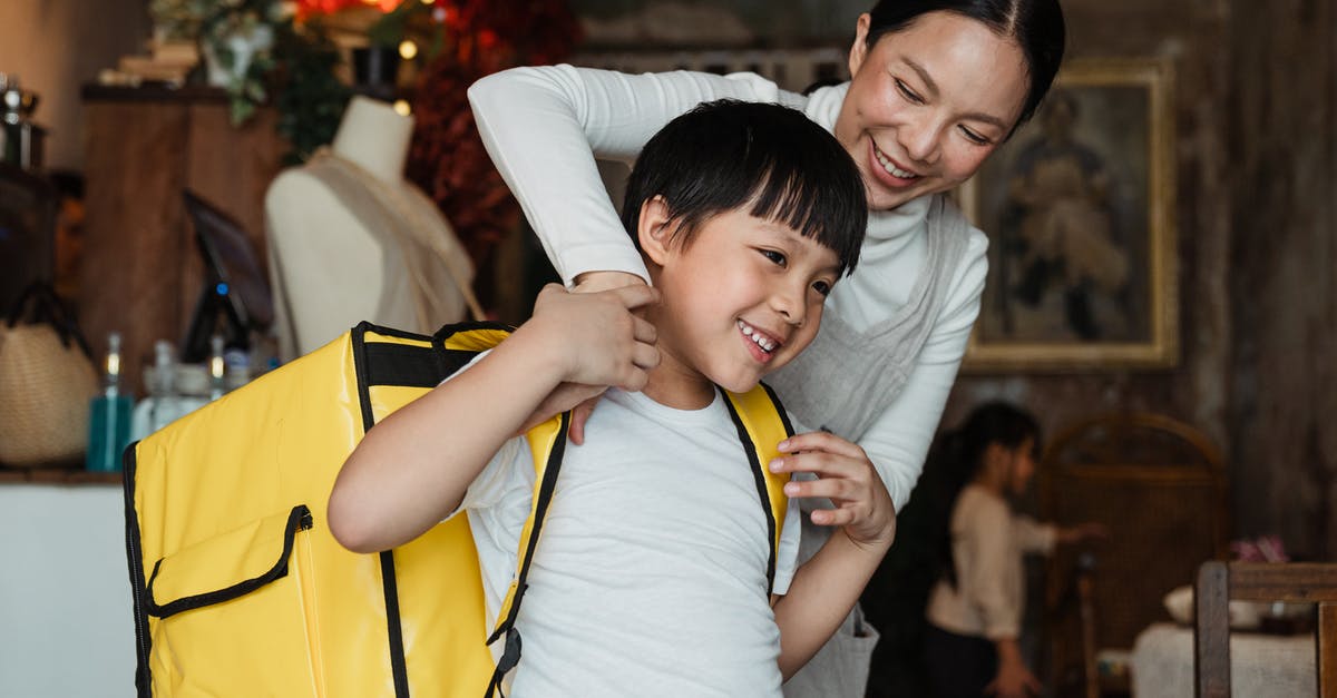 How does Mother Base staff morale work? - Happy female cafeteria employee putting on big yellow thermo bag on shoulders of positive child in casual wear working as food courier and looking away