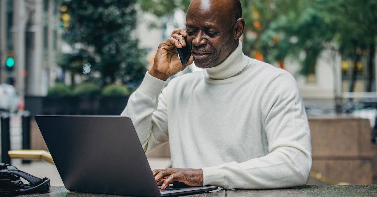How does personality reputation work? - Concentrated African American man talking on mobile phone while working on laptop on city street How does personality reputation work? - Concentrated African American man talking on mobile phone while working on laptop on city street