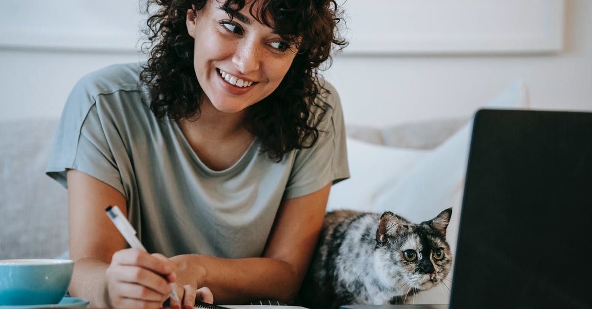 How does pet insurance work for leagues? - Crop young positive female smiling and taking notes in organizer while cat watching on netbook at table at home How does pet insurance work for leagues? - Crop young positive female smiling and taking notes in organizer while cat watching on netbook at table at home